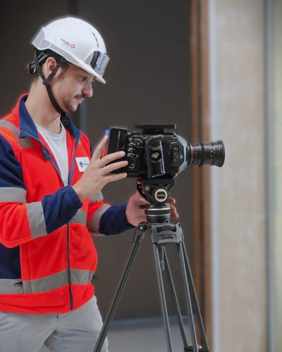 Axel Milon en tournage sur un chantier : casque, gilet haute visibilité, caméra sur trépied